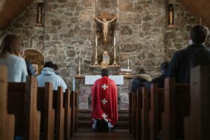 a priest with his back to a congregation kneels before the Eucharist