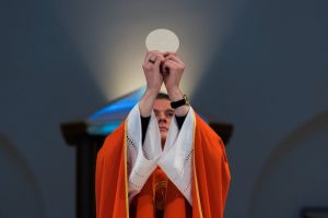 priest-lifting-up-eucharist-at-altar-during-mass