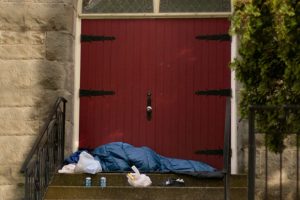 person-sleeping-bag-church-steps-red-door