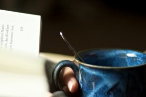 hand-holding-coffee-cup-next-to-open-book