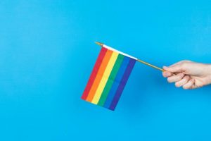 hand-holds-rainbow-flag-against-blue-background