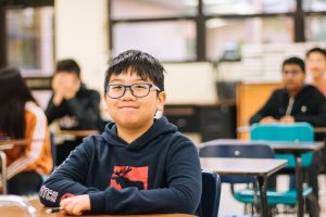 a-boy-sits-at-a-desk-and-smiles