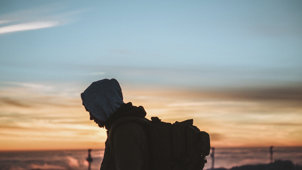 man-in-hoodie-with-backpack-looking-at-sunset