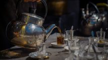 Person pouring black tea into a small glass.