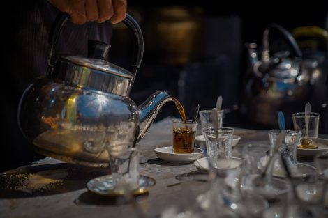 Person pouring black tea into a small glass.