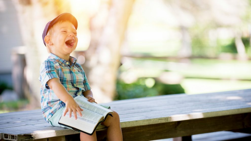 Child sitting on a bench with a bible and smiling