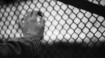 Black and white image of a hand behind chain link fence