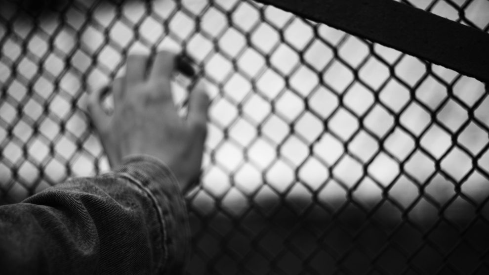 Black and white image of a hand behind chain link fence