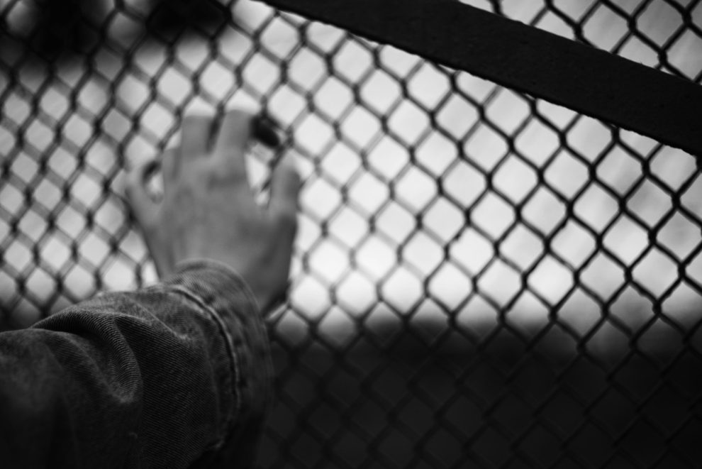 Black and white image of a hand behind chain link fence