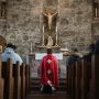 a priest with his back to a congregation kneels before the Eucharist